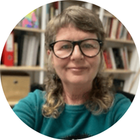 Headshot of Professor Robyn Martin in front of a bookshelf. She is wearing glasses and a green jumper. 