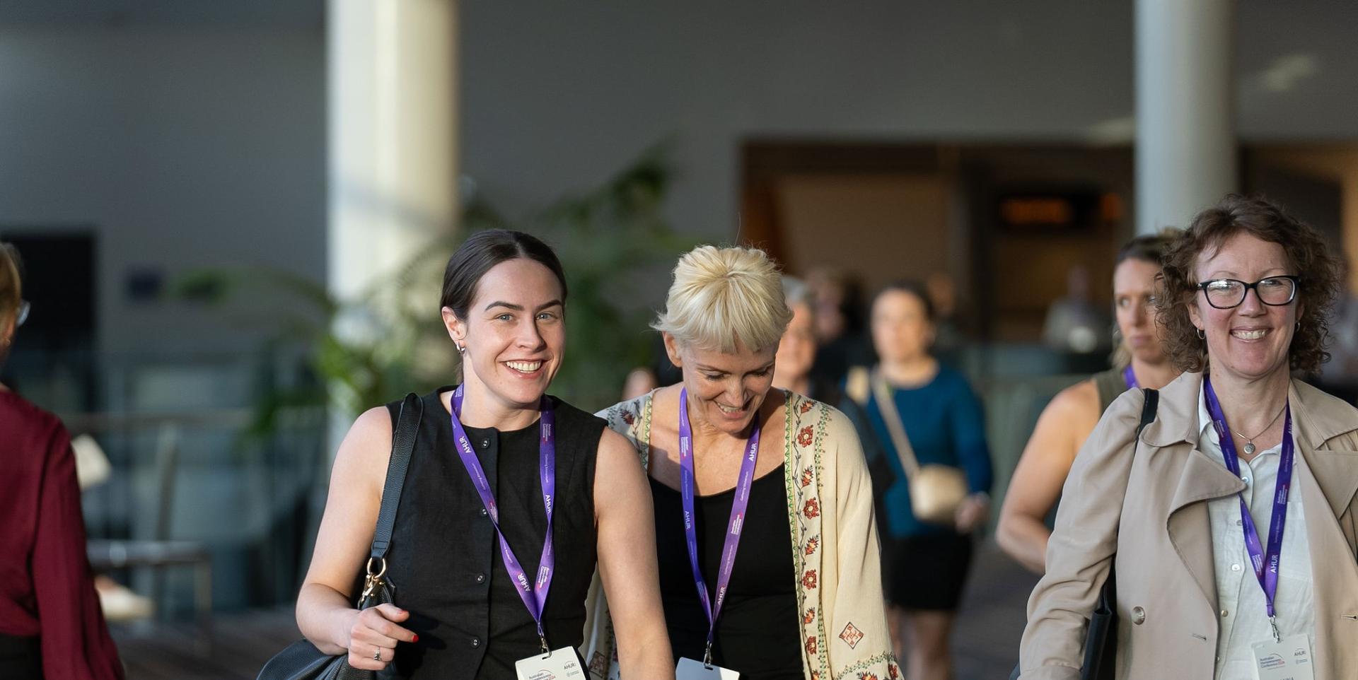 Group of women laughing and smiling as they walk together in a conference exhibition space at Australian Homelessness Conference 2024
