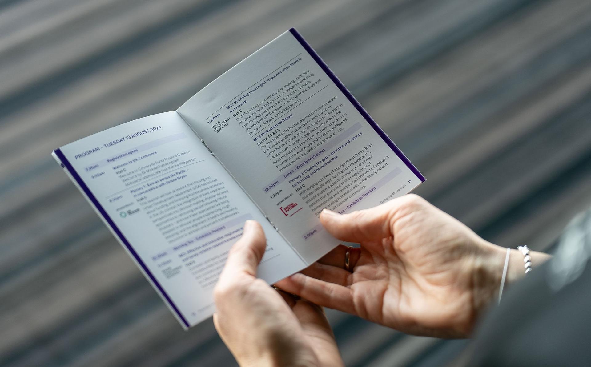 Person's hands holding a pocket program for Australian Homelessness Conference 2024