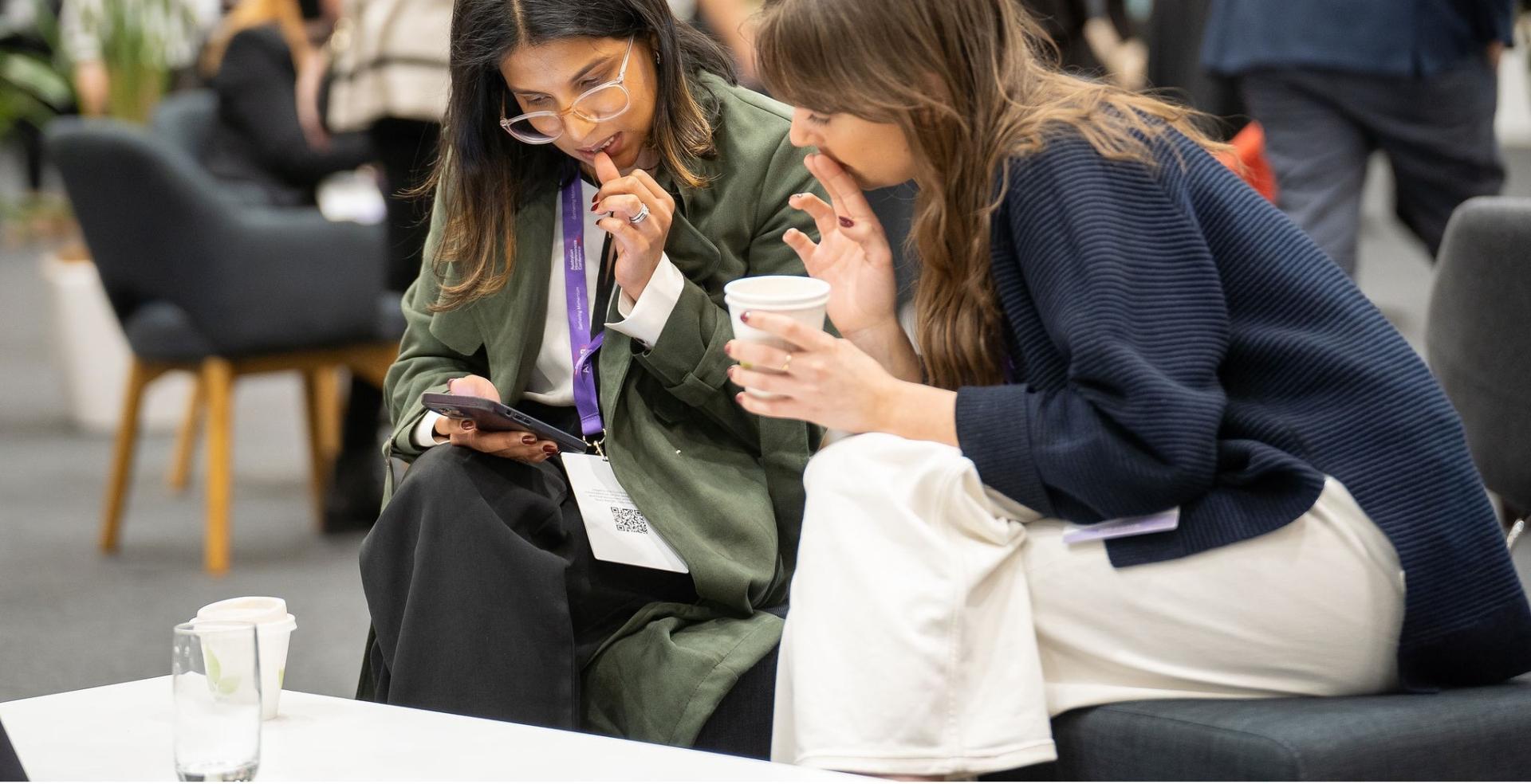 Two women sitting down at a low coffee table at Australian Homelessness Conference 2024 looking at a phone.